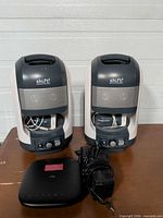 Front view of both Shift3 speakers, internal bays open showing transmitter; ZTE device and power adapters visible