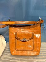 Front view of crocodile-embossed handbag with front pocket and silver heart hardware