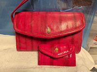 Front view of red clutch and matching key holder wallet showing exterior finish and emblem