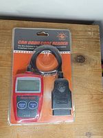 Front of sealed blister pack showing red handheld code reader and black OBDII cable