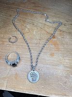 Necklace with cupcake pendant, blue stone ring, open-work band ring on wooden surface