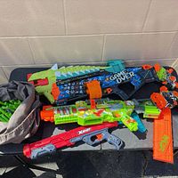 Overview showing three blasters, magazine and bag of darts on table