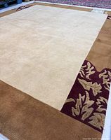 Full view of rug showing central beige field and tan border with burgundy leaf motif corner