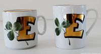 Front view of both mugs showing gold E and clover motifs