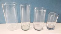 Four clear cylindrical glass vases standing upright showing relative sizes