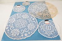 All four round white lace doilies laid out showing size variation and slight discoloration on one