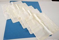 Five pale yellow cloth serviettes laid out on blue background