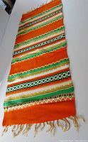 Full view of woven orange runner with multicolour stripes and fringe