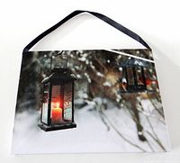 Front view of canvas picture showing lantern with lit candle and black ribbon hanger