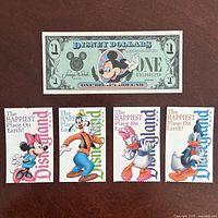 Front of Disney Dollar and four illustrated ticket fronts