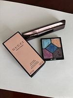 Front view of boxed Gucci nail polish, Hourglass foundation stick, Dior eyeshadow refill