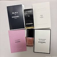 Five Chanel items laid out: nail polish box, four perfume sample sleeves, nail polish bottle centered