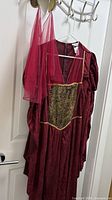 Full view of burgundy Renaissance dress on hanger with headband and veil above