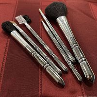 Six chrome-handled T. LeClerc brushes laid out on red fabric