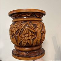 Side view of carved wood planter showing floral and human figure relief