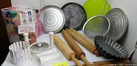 Group shot of rolling pins, flan pans, doll cake mold box, onion blossom maker parts, strainer, silicone splash guard