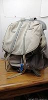 Front view showing grey canvas body, leather straps, blue toggle, flap