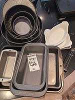 Stack of springform pans, loaf pans, square pan, ceramic dishes and measuring spoons