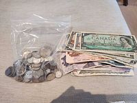 Bag of assorted coins beside stacked Canadian banknotes