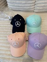 Four Mercedes AMG Petronas Lewis Hamilton caps in navy, aqua, pink, purple displayed front view showing Mercedes star logos