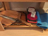 Overall lot showing pizza peel, skewers, mandoline, silicone mat, metal grate on shelf