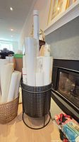 Perforated metal holder filled with multiple rolled posters/maps; wicker basket with more rolls beside