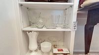 Overall view of two shelves showing vases, candy dish, pedestal stand, milk-glass vase, ceramic bowl and boxed ramekins