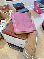 Stacked red and brown hardcover books on top of box containing additional volumes