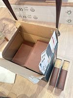 Open cardboard box with several brown hardcover books inside and two volumes outside