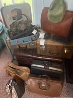 Group shot of assorted vintage suitcases, bags, floral handbag inside open blue case, green corduroy cap