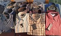 Overview of all 16 folded shirts on table showing variety of patterns and tags