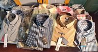 Front view of 19 packaged men’s shirts on table showing assorted patterns and attached tags