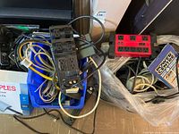 Assorted surge protectors, cords and Wi-Fi extender boxes in blue bin and surrounding floor