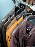 Five leather jackets hanging on rack showing varied colors and leather finishes