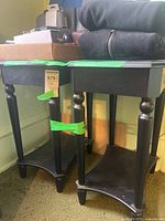 Two black wood side tables side by side showing tops, legs, drawer fronts and lower shelves