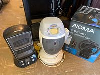 Front view showing black NOMA heater, white Honeywell heater on base, and boxed NOMA fan
