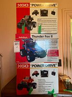 Stacked view of three boxed remote-controlled trucks showing GO Power Drive black, RadioShack Thunder Fox II blue, and GO Power Drive red models