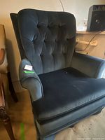Front view of dark upholstered armchair showing button-tufted back, padded arms and seat