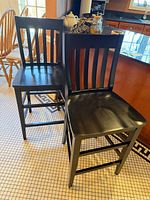 Both black wooden bar stools showing fronts and seats