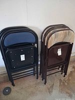 Two stacks of folding chairs showing cushioned backs (blue and striped) and metal frames
