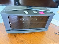 Front view showing overall shape, glass doors, finish, TV on top for scale