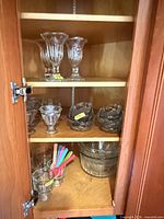 Cabinet shelves with tall parfait cups, dessert cups, banana boat dishes, tumblers, plastic spoons, serving bowls