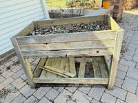 Front view of rectangular raised wood planter showing planting box with leaf debris and lower slatted shelf