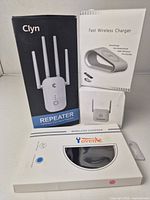 Front view of three boxed items showing Clyn repeater, unbranded fast wireless charger, and Yovente wireless charger