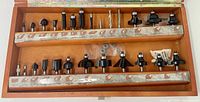 Open wooden case displaying two rows of router bits (26 total) and accessories