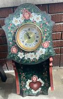 Front view of painted wooden wall clock showing floral and heart design and Roman-numeral dial