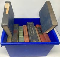 Blue plastic bin containing multiple hardcover books; two additional books leaning against bin edges