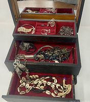 Jewelry box open showing contents: assorted costume jewelry pieces in red-lined tiers