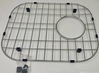 Top view of stainless steel sink grid showing drain opening, installed rubber feet, spare bumpers bag