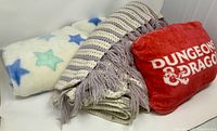 Overview of three items: star blanket, striped knit throw, red D&D pillow